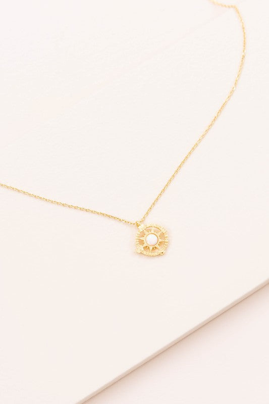 The Pixum Compass Stone Necklace, featuring a thin gold chain and a pendant with a turquoise stone set in a circular gold disc, captures the bohemian jewelry essence beautifully against a light background.