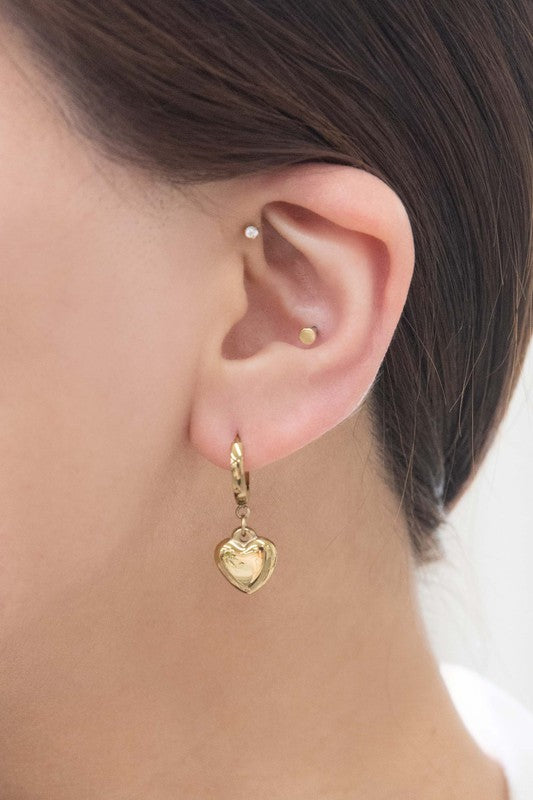 The Adore Hoop Earrings are crafted from stainless steel, plated in 14k gold, and feature charming heart-shaped pendants that dangle elegantly against a pristine white background.