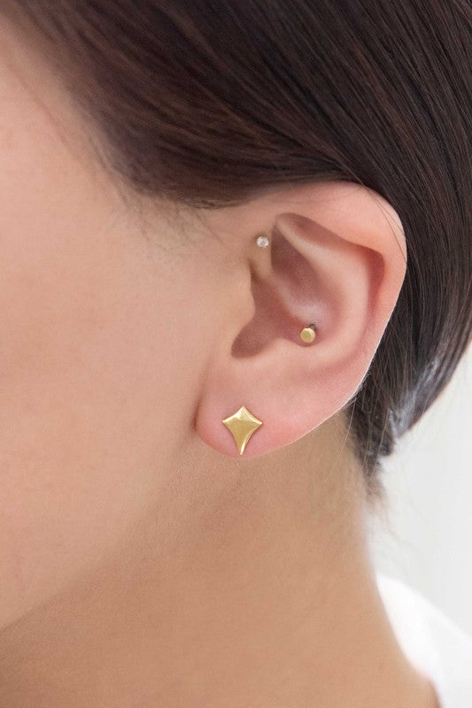 The Sparks Stud Earrings are charming, small diamond-shaped pieces crafted from 14k gold plated material. They are hypoallergenic and stand out beautifully against a white background.