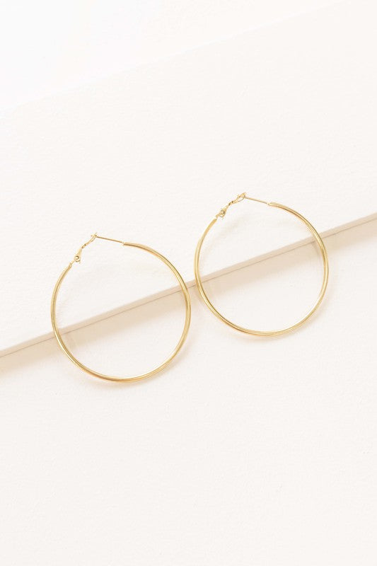 A pair of Simplicity Hoop Earrings, crafted with 14k gold plating, are elegantly displayed on a pristine white surface.