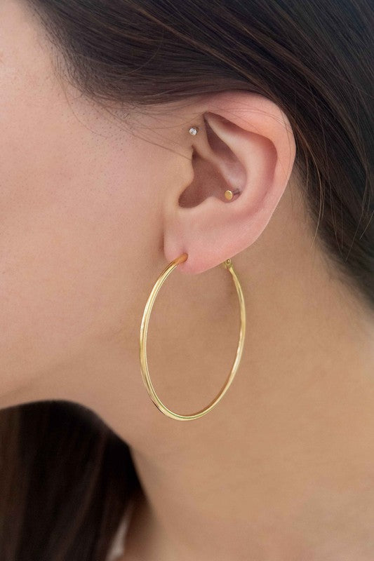 A pair of Simplicity Hoop Earrings, crafted with 14k gold plating, are elegantly displayed on a pristine white surface.