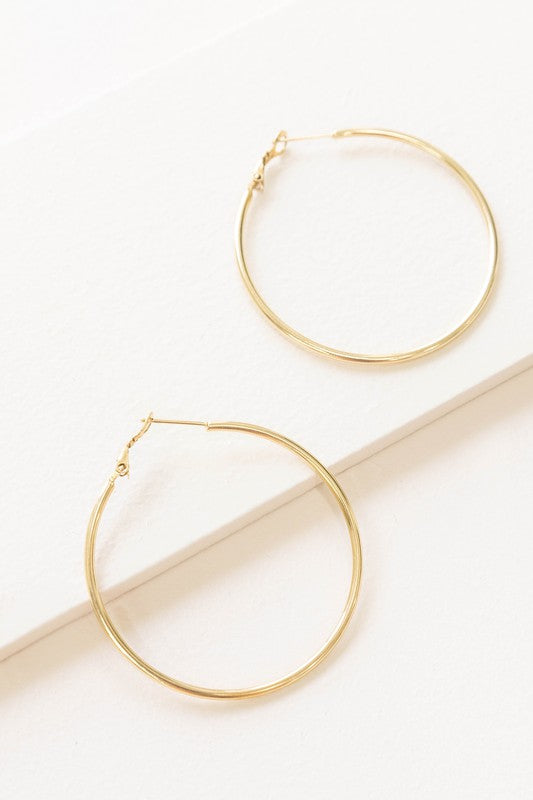 A pair of Simplicity Hoop Earrings, crafted with 14k gold plating, are elegantly displayed on a pristine white surface.