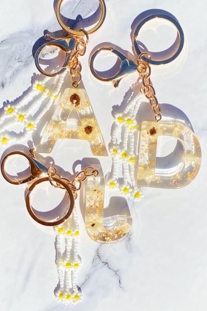 Baby Daisy Initial Key Chain alphabet keychains with real daisy flowers and gold flakes on a marble surface.