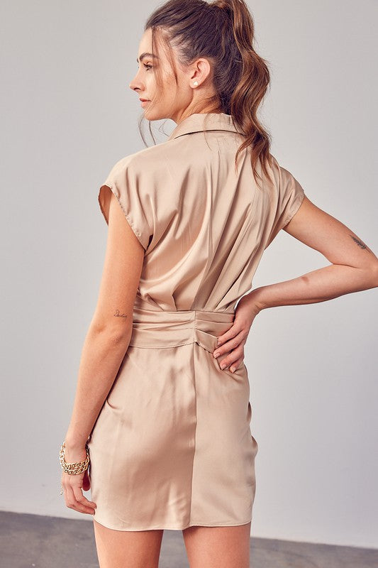 A person in a Collar Button Up Front Tie Dress with beige colors and white boots is standing on a concrete floor in front of a plain wall.