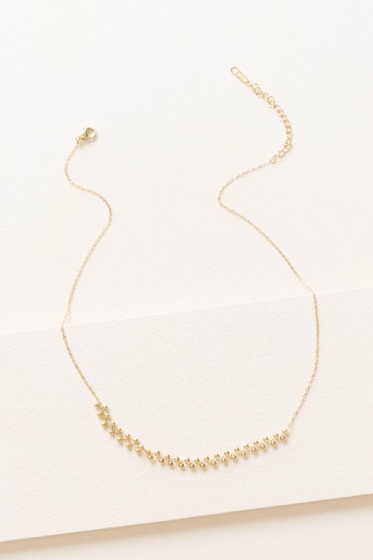 The Samba Charm Necklace is an elegant accessory adorned with small, evenly spaced floral-shaped charms that rest gracefully on a white background. Made from 14k gold-plated stainless steel, this necklace embodies timeless style and sophistication.