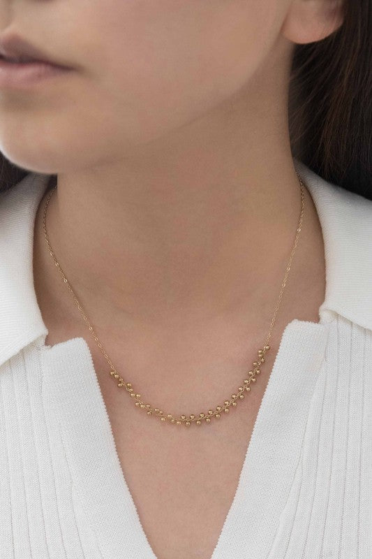 The Samba Charm Necklace is an elegant accessory adorned with small, evenly spaced floral-shaped charms that rest gracefully on a white background. Made from 14k gold-plated stainless steel, this necklace embodies timeless style and sophistication.