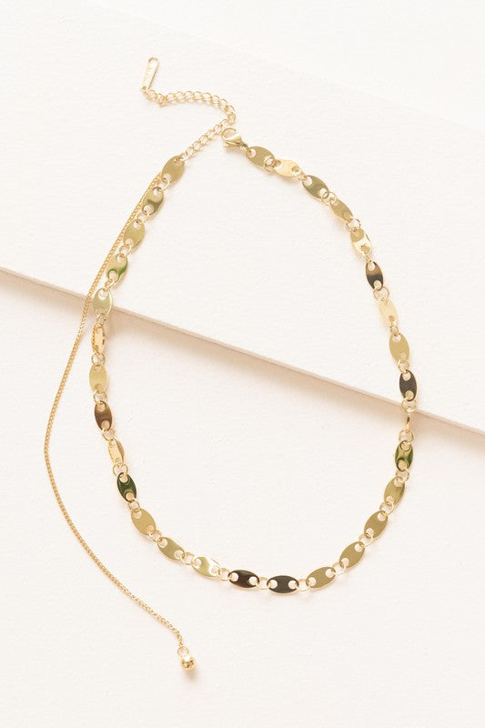 The Oval Chain Necklace, featuring a 14k gold plated finish with oval links and an adjustable clasp, is elegantly displayed on a white surface, highlighting its sophisticated design and stainless steel durability.