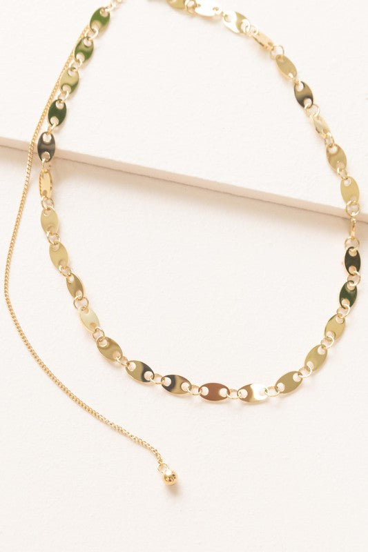 The Oval Chain Necklace, featuring a 14k gold plated finish with oval links and an adjustable clasp, is elegantly displayed on a white surface, highlighting its sophisticated design and stainless steel durability.