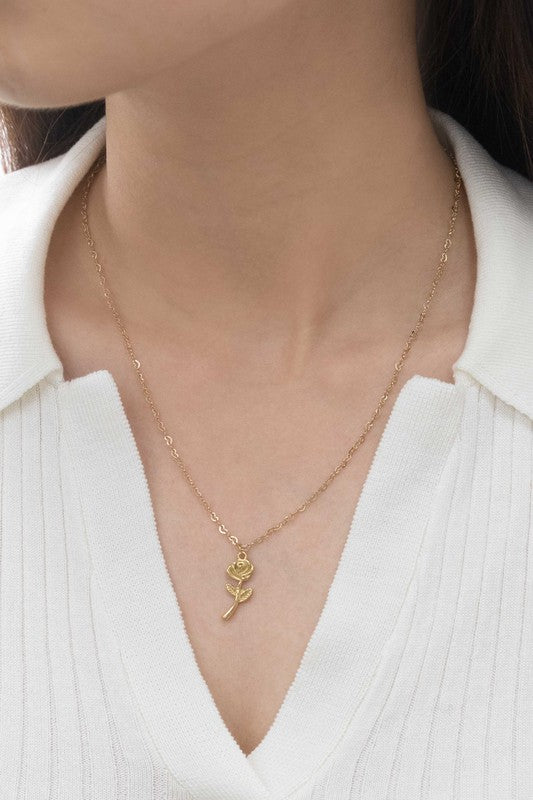 The La Vie En Rose Charm Necklace boasts a gold pendant intricately designed in the form of a rose, elegantly hanging against a subtle background. This classic accessory is 14k gold plated, providing sophistication to any outfit.