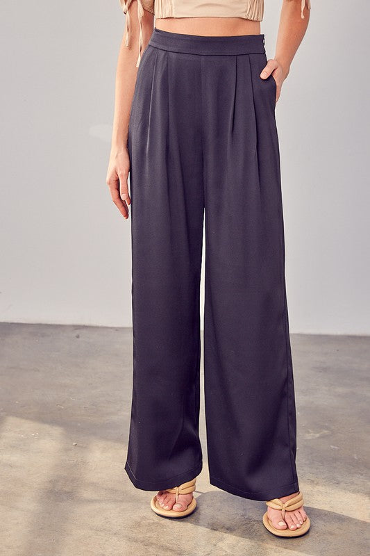 A person wearing Wide Leg Pants and sandals stands on a concrete floor, showcasing a versatile wardrobe with their flowing silhouette.