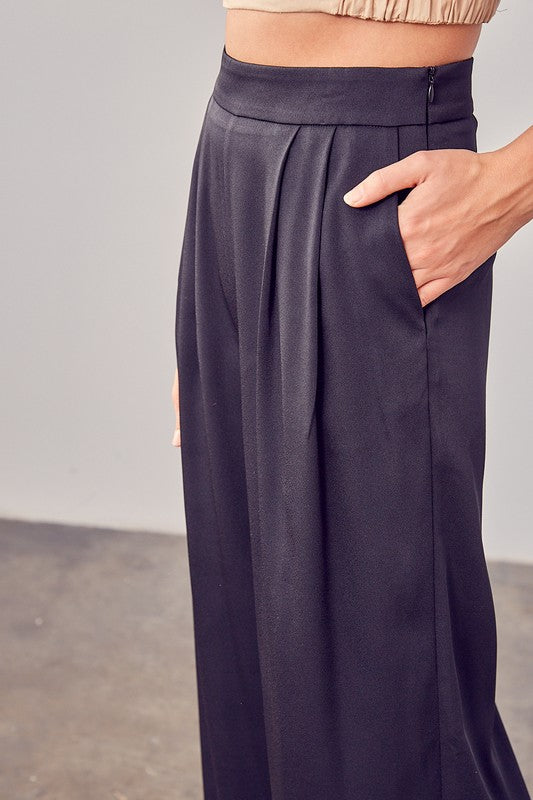 A person wearing Wide Leg Pants and sandals stands on a concrete floor, showcasing a versatile wardrobe with their flowing silhouette.