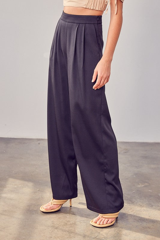 A person wearing Wide Leg Pants and sandals stands on a concrete floor, showcasing a versatile wardrobe with their flowing silhouette.