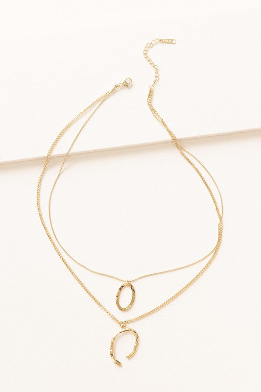 Introducing the Ithaca Layered Necklace, a stunning piece crafted from 14k gold plating. This necklace features two delicate chains adorned with a small oval pendant and a chic horseshoe pendant.