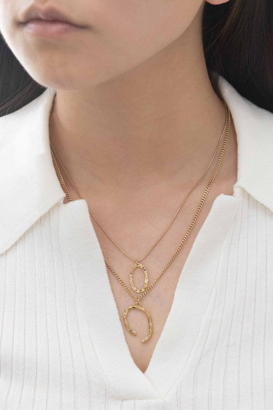 Introducing the Ithaca Layered Necklace, a stunning piece crafted from 14k gold plating. This necklace features two delicate chains adorned with a small oval pendant and a chic horseshoe pendant.