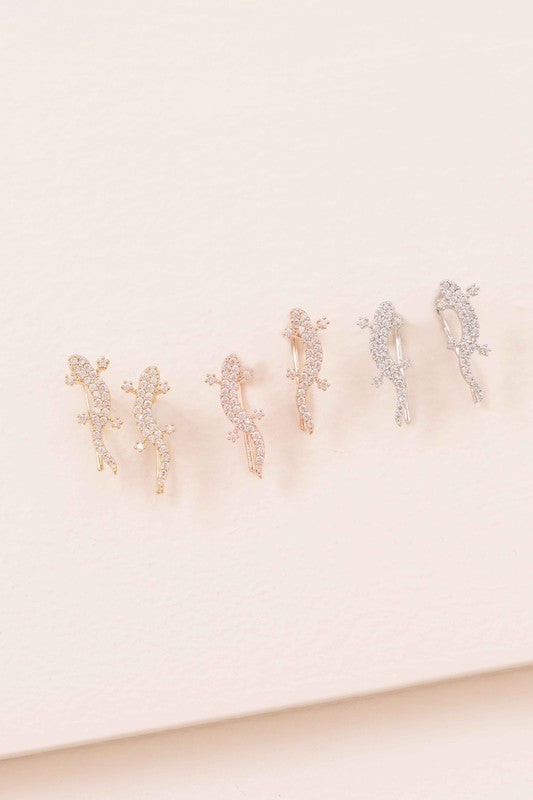 Three pairs of Lizard Ear Pin Earrings, featuring captivating stone-studded designs in gold, rose gold, and silver-plated brass jewelry, are elegantly presented on a light surface.