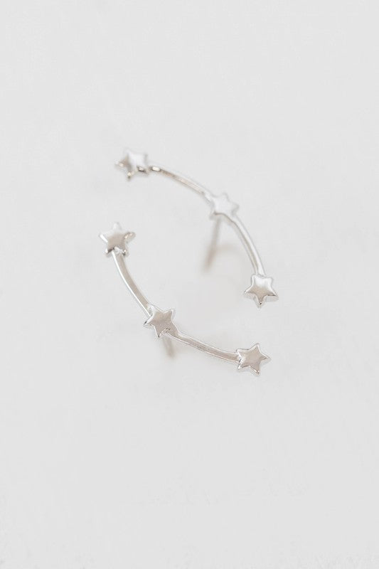 The Starry Crawler earrings, crafted from sterling silver and featuring a crescent shape adorned with small star accents, rest against a white background.