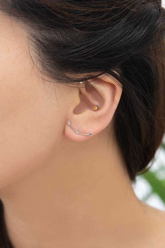 The Starry Crawler earrings, crafted from sterling silver and featuring a crescent shape adorned with small star accents, rest against a white background.