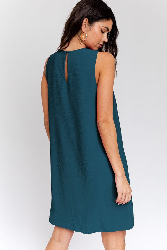 A woman elegantly poses in the Sleeveless V-Neck Dress, highlighting a chic and stylish appearance against a minimalistic backdrop. This versatile wardrobe piece epitomizes both elegance and simplicity.