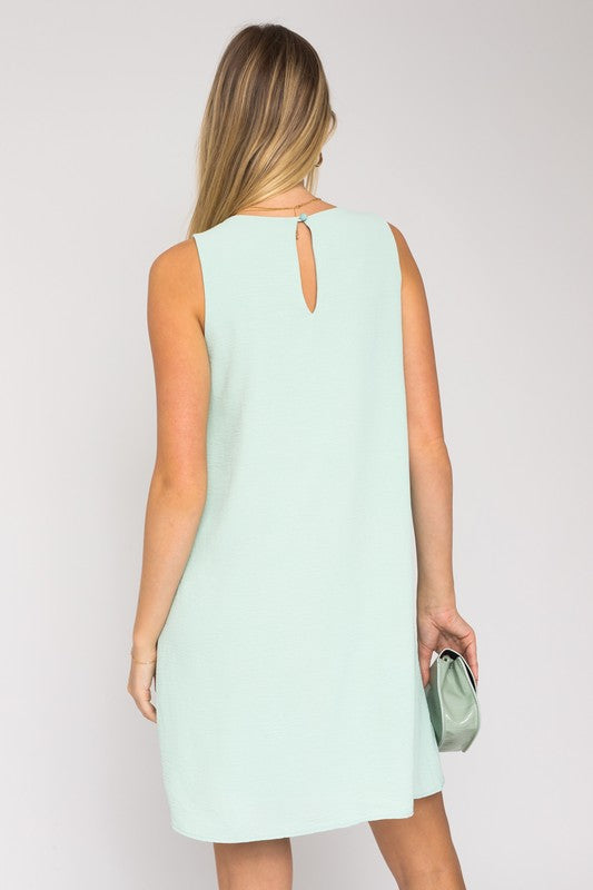 A woman elegantly poses in the Sleeveless V-Neck Dress, highlighting a chic and stylish appearance against a minimalistic backdrop. This versatile wardrobe piece epitomizes both elegance and simplicity.