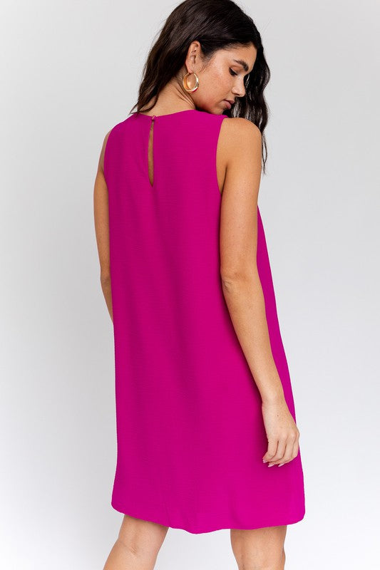 A woman elegantly poses in the Sleeveless V-Neck Dress, highlighting a chic and stylish appearance against a minimalistic backdrop. This versatile wardrobe piece epitomizes both elegance and simplicity.