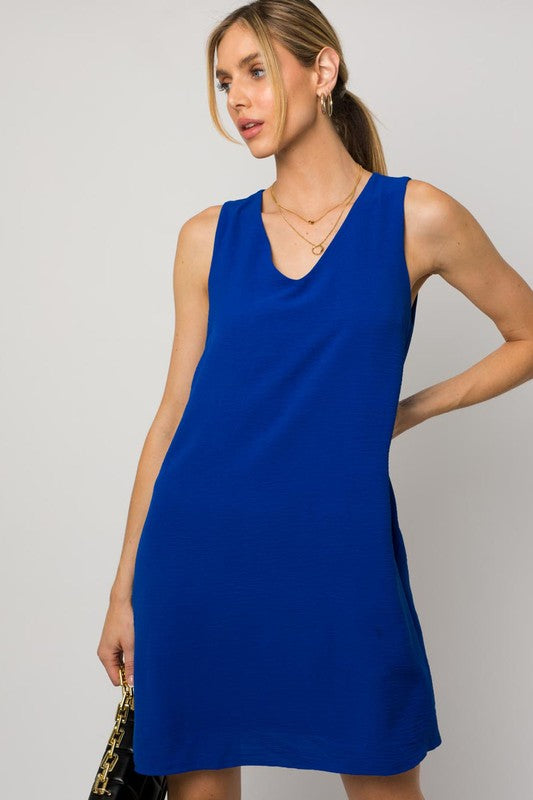 A woman elegantly poses in the Sleeveless V-Neck Dress, highlighting a chic and stylish appearance against a minimalistic backdrop. This versatile wardrobe piece epitomizes both elegance and simplicity.