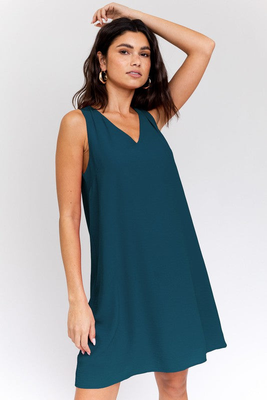 A woman elegantly poses in the Sleeveless V-Neck Dress, highlighting a chic and stylish appearance against a minimalistic backdrop. This versatile wardrobe piece epitomizes both elegance and simplicity.