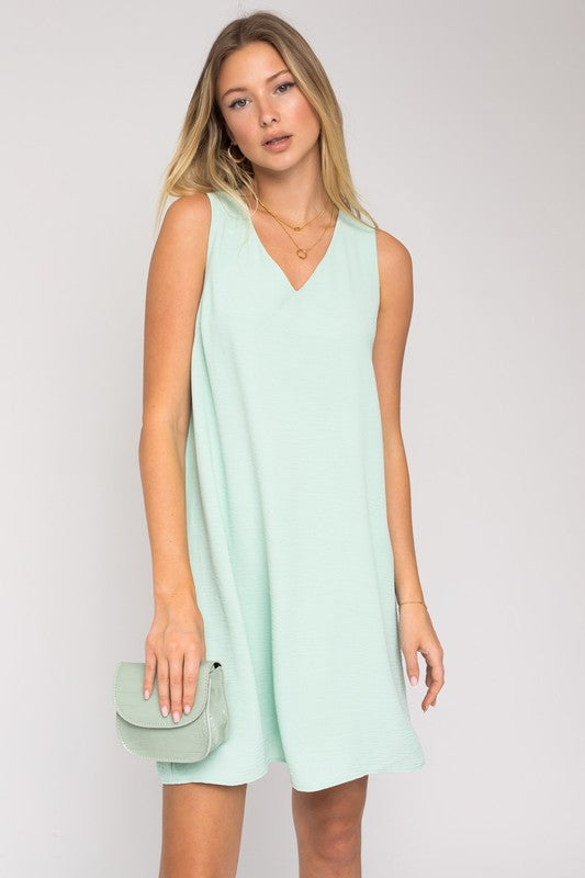 A woman elegantly poses in the Sleeveless V-Neck Dress, highlighting a chic and stylish appearance against a minimalistic backdrop. This versatile wardrobe piece epitomizes both elegance and simplicity.