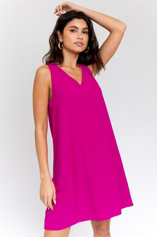 A woman elegantly poses in the Sleeveless V-Neck Dress, highlighting a chic and stylish appearance against a minimalistic backdrop. This versatile wardrobe piece epitomizes both elegance and simplicity.