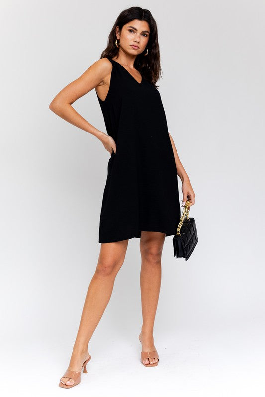 A woman elegantly poses in the Sleeveless V-Neck Dress, highlighting a chic and stylish appearance against a minimalistic backdrop. This versatile wardrobe piece epitomizes both elegance and simplicity.