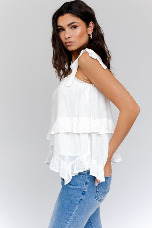 Woman wearing a Sleeveless Asymmetrical Hem Line Tiered Top and blue jeans, standing against a plain background.