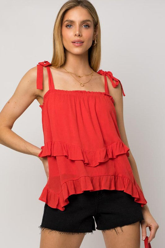 Woman wearing a Sleeveless Asymmetrical Hem Line Tiered Top and blue jeans, standing against a plain background.