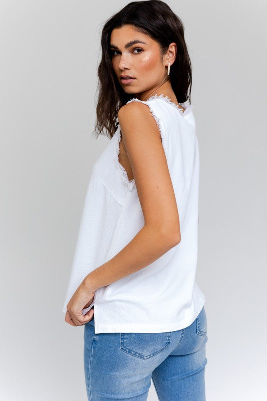 Dressed in a stylish Edgy Frayed Top paired with blue jeans, an individual sits on a stool against a simple backdrop, poised for casual outings.