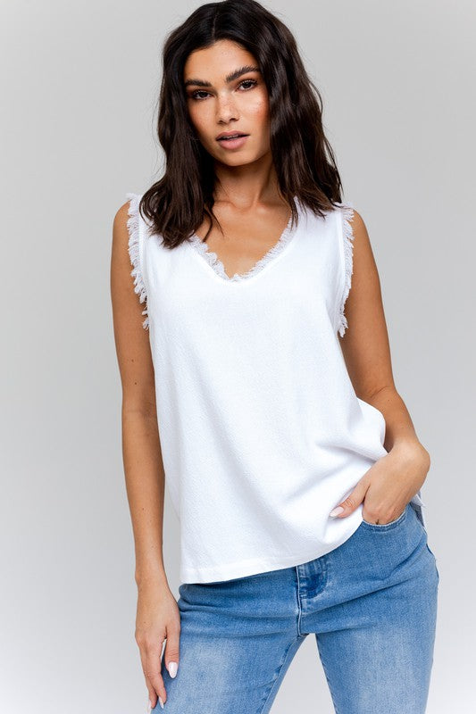 Dressed in a stylish Edgy Frayed Top paired with blue jeans, an individual sits on a stool against a simple backdrop, poised for casual outings.