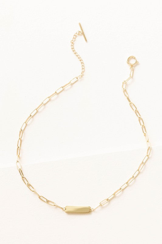 Plate Oval Chain Necklace showcases a bar pendant and sleek toggle clasp, plated with 14k gold on high-quality stainless steel against a light background.