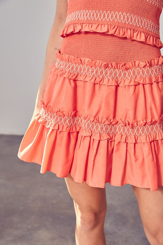 A person wearing a coral-colored dress from the Tiered Ruffle Skirt collection with white stitching details, radiating playful and feminine charm.