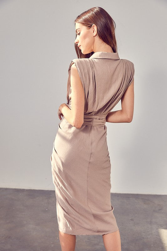 A woman in a white Sleeveless Button Front Tie Dress stands in a minimalist room with concrete flooring and neutral-colored walls. She has long brown hair and wears a necklace, making it perfect for summer gatherings.