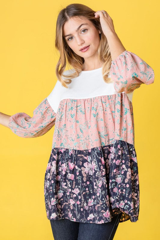 A person wearing a Three Tiered Bishop Sleeve Paisley Floral Tunic and jeans stands gracefully against a vivid yellow background.