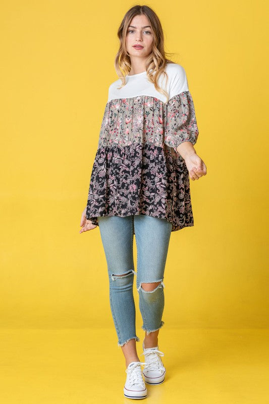 A person wearing a Three Tiered Bishop Sleeve Paisley Floral Tunic and jeans stands gracefully against a vivid yellow background.