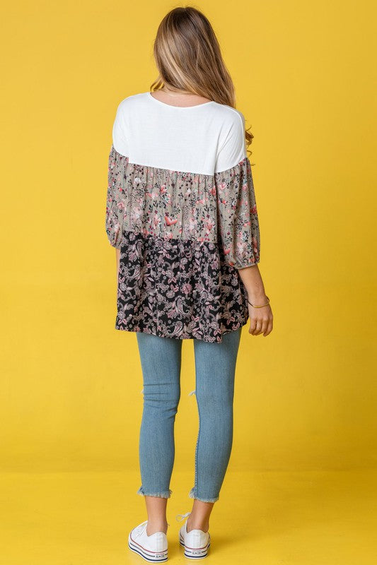 A person wearing a Three Tiered Bishop Sleeve Paisley Floral Tunic and jeans stands gracefully against a vivid yellow background.