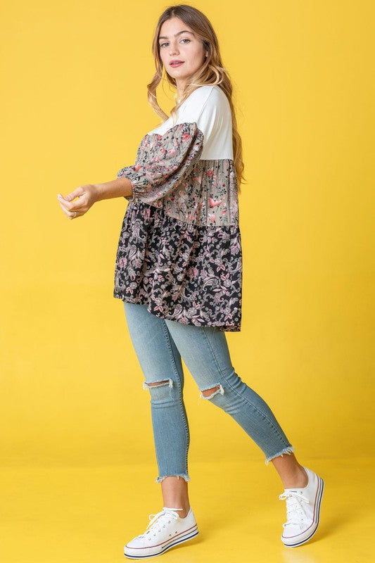 A person wearing a Three Tiered Bishop Sleeve Paisley Floral Tunic and jeans stands gracefully against a vivid yellow background.