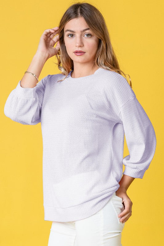 Wearing a Plus Solid Waffle Knit Top and white pants, a woman stands gracefully against a vibrant yellow background.