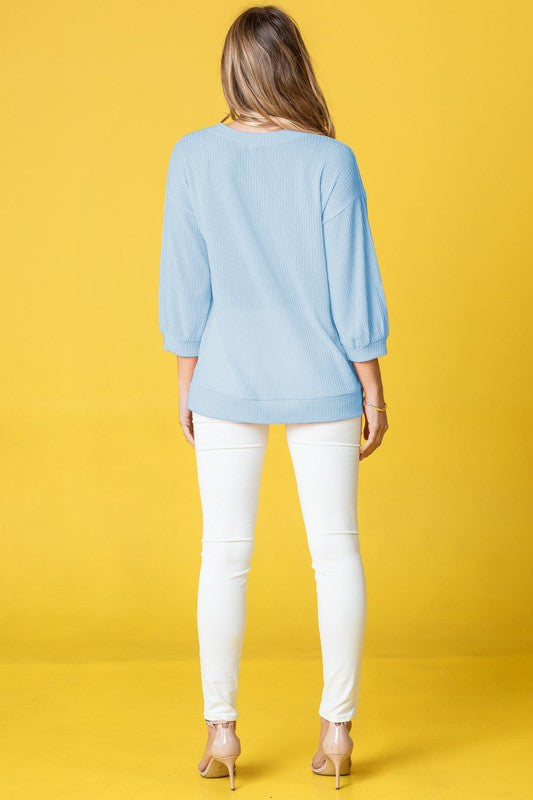 Wearing a Plus Solid Waffle Knit Top and white pants, a woman stands gracefully against a vibrant yellow background.