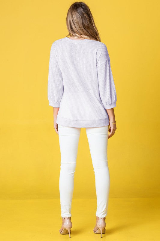 Wearing a Plus Solid Waffle Knit Top and white pants, a woman stands gracefully against a vibrant yellow background.