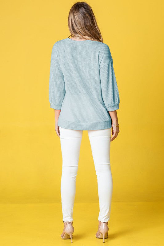 Wearing a Plus Solid Waffle Knit Top and white pants, a woman stands gracefully against a vibrant yellow background.