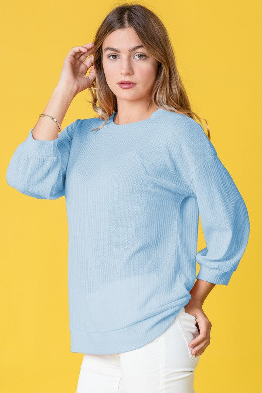 Wearing a Plus Solid Waffle Knit Top and white pants, a woman stands gracefully against a vibrant yellow background.