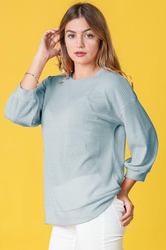 Wearing a Plus Solid Waffle Knit Top and white pants, a woman stands gracefully against a vibrant yellow background.