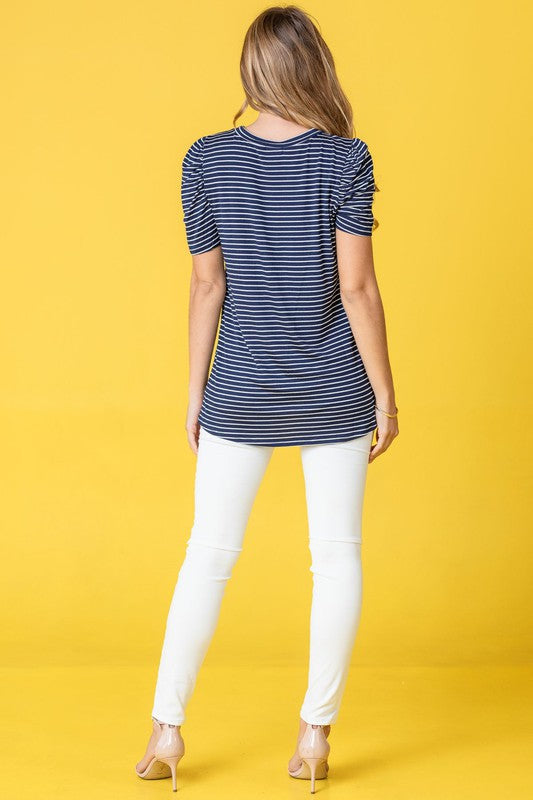 A woman presents the Stripe Puff Ruched Sleeve Top, a navy and white shirt with ruched sleeves, against a vibrant yellow background.