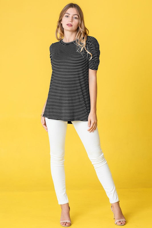 A woman presents the Stripe Puff Ruched Sleeve Top, a navy and white shirt with ruched sleeves, against a vibrant yellow background.