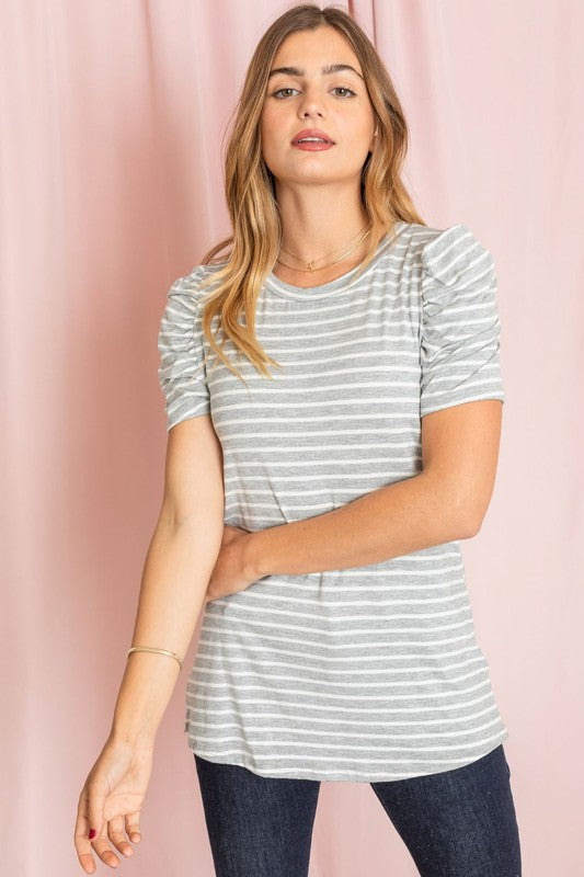 A woman presents the Stripe Puff Ruched Sleeve Top, a navy and white shirt with ruched sleeves, against a vibrant yellow background.