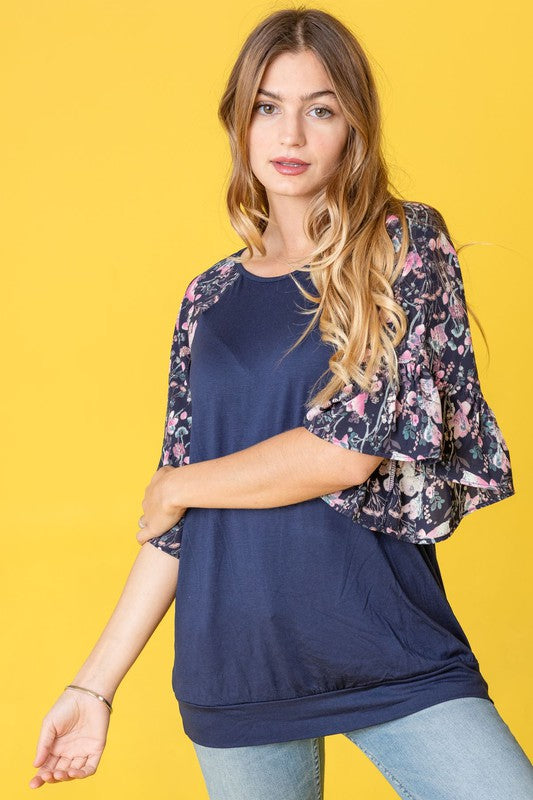 A woman with long hair is wearing the Ruffle Print Sleeve Tunic in navy blue, standing against a yellow background.